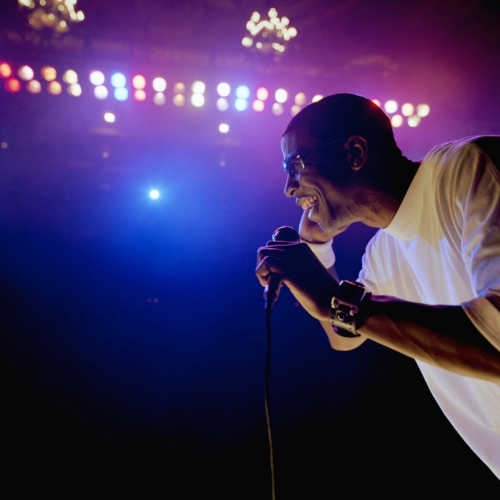 A comedian passionately performing onstage, microphone in hand, with a backdrop of colorful stage lights